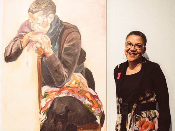 Lauren Y. Casteel stands next to a painting by artist, Jordan Casteel