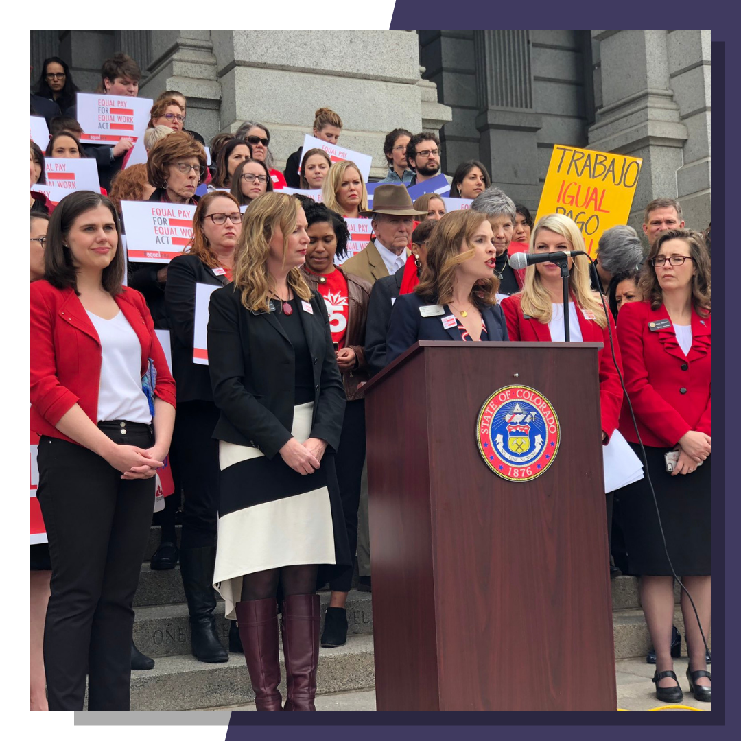 WFCO Vice President of Programs, Louise Myrland, speaks at the steps of the Denver capitol in support of Equal Pay Act. Many women stand behind her holding Equal Pay Act signs