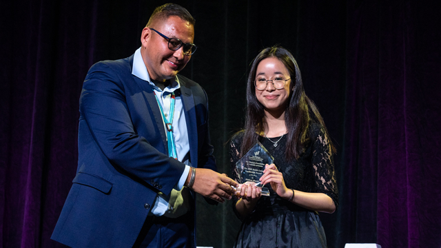 Shelnna Huynh of Denver stands on stage with WFCO Trustee Ray Foxworth with her Dottie Lamm Award 